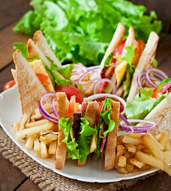 Club Sandwich mit Käse, Gurke, Tomate, geräuchertem Fleisch und Salami. Serviert mit Pommes Frites.