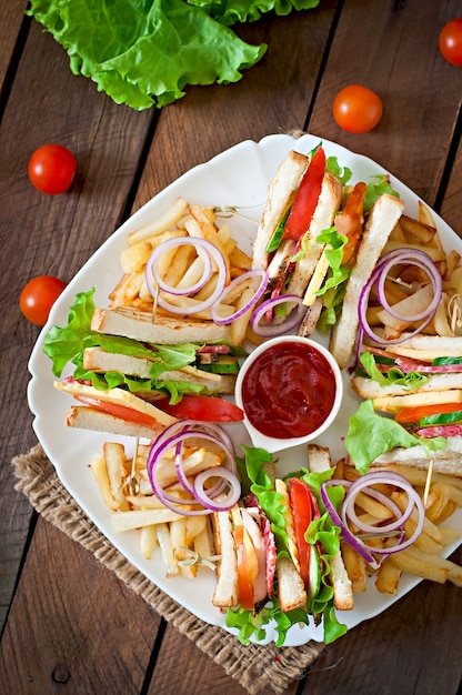 Club Sandwich mit Käse, Gurke, Tomate, geräuchertem Fleisch und Salami. Serviert mit Pommes Frites.