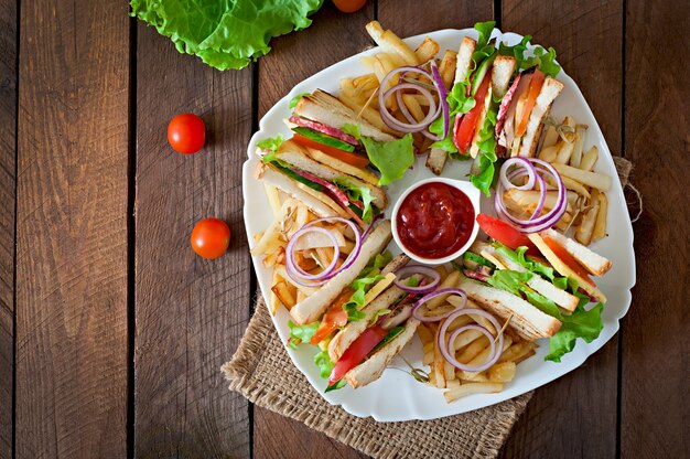 Club Sandwich mit Käse, Gurke, Tomate, geräuchertem Fleisch und Salami. Serviert mit Pommes Frites.