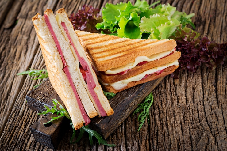 Kostenlose Foto club sandwich - panini mit schinken und käse auf holztisch. picknick essen.