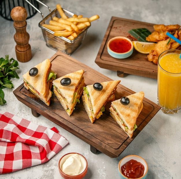 Club Sandwiches auf einem Holzbrett mit Pommes Frites und Orangensaft.