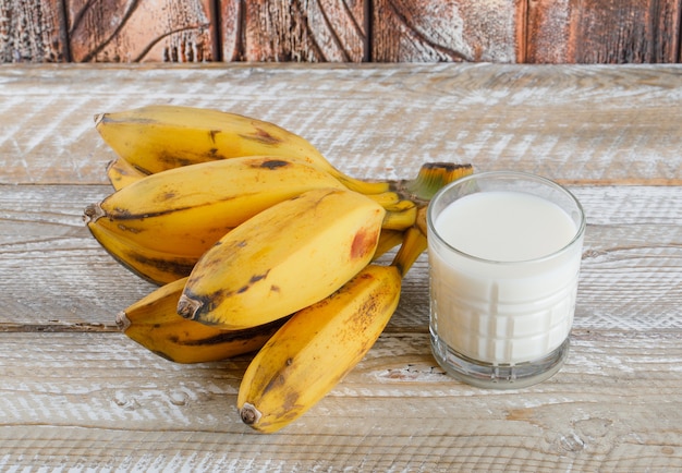 Cluster von Bananen mit Milch auf hölzerner, hoher Winkelansicht.