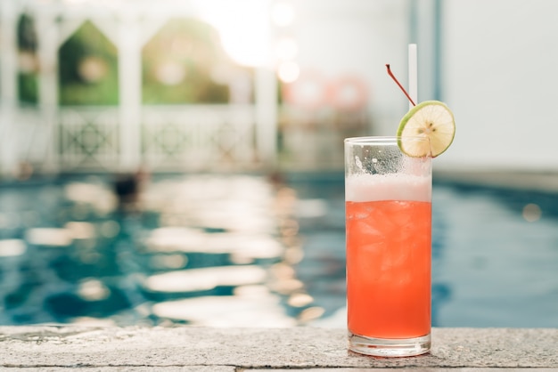Cocktail am Rande des Schwimmbades. Roter Cocktail mit Orangenscheibe auf dem Hintergrund des Schwimmbads. Vintage Effekt Stil Bilder.