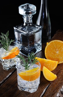 Cocktail klassischer dry gin mit tonic und orangenschale mit einem rosmarinzweig auf einem holzbrett mit saftigen orangenscheiben