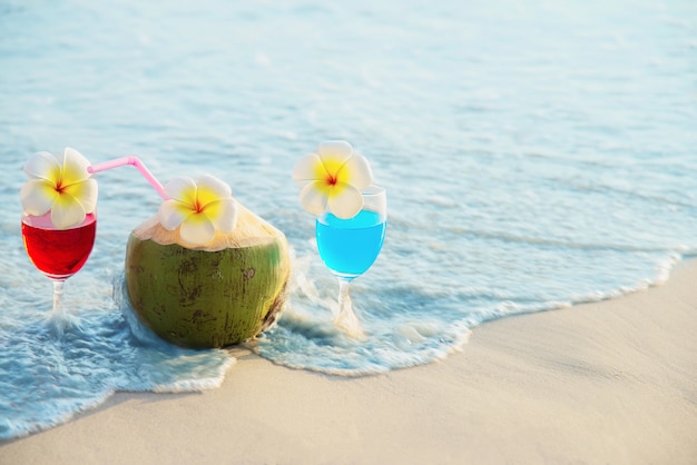 Cocktailgläser mit Kokosnuss und Ananas auf sauberem Sand setzen - Frucht und Getränk auf Seestrand auf den Strand