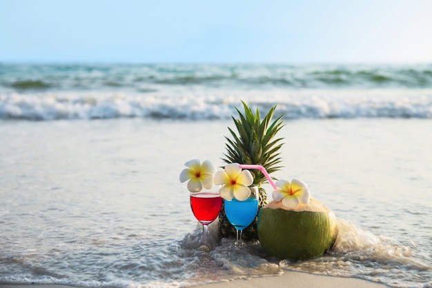 Cocktailgläser mit Kokosnuss und Ananas auf sauberem Sand setzen - Frucht und Getränk auf Seestrand auf den Strand
