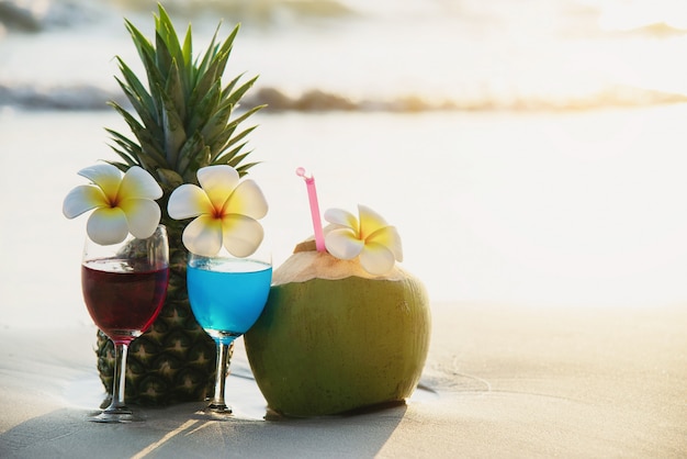 Cocktailgläser mit Kokosnuss und Ananas auf sauberem Sand setzen - Frucht und Getränk auf Seestrand auf den Strand