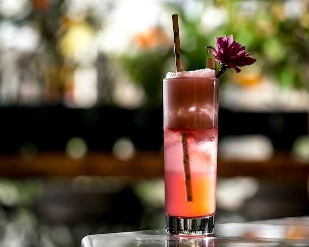 Cocktailglas garniert mit Blumen- und Papierstroh in der Nähe der Terrasse