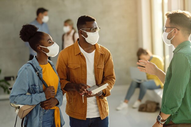 College-Studenten, die schützende Gesichtsmasken tragen, während sie sich in einer Lobby unterhalten