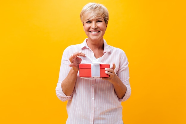 Coole erwachsene Dame lächelt und hält Geschenkbox auf orange Hintergrund