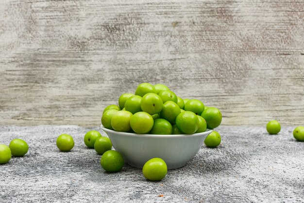 Coole Greengages in einer weißen Schüssel auf Grunge braun und grau, Seitenansicht.