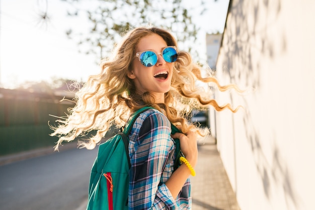 Coole stilvolle lächelnde glückliche blonde Frau, die in Straße mit Rucksack geht