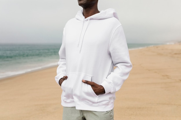 Cooler afroamerikanischer Mann im weißen Hoodie bei einem Strand-Winter-Shooting