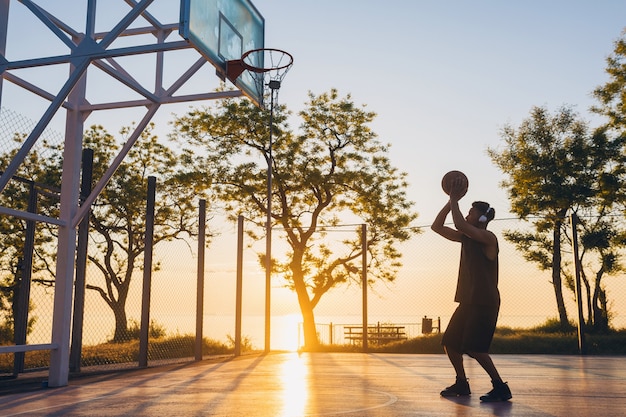 Cooler junger Mann, der Sport macht, Basketball bei Sonnenaufgang spielt