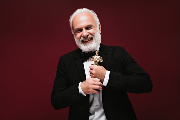 Cooler Mann im schwarzen Anzug lacht und hält Oscar-Statuette