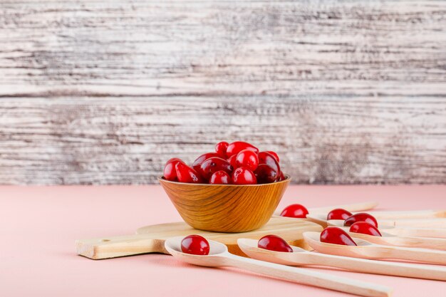 Cornel Beeren in Löffeln und Schüssel mit Schneidebrett Seitenansicht auf rosa und Holz