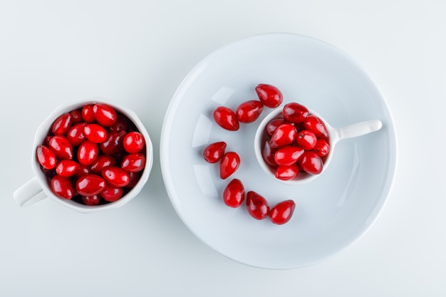 Cornel beeren in schaufel, teller und tasse auf weiß. draufsicht.