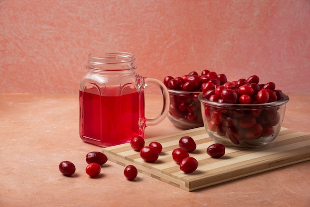 Cornels in Glasschale und Saft in einem Glas auf einem rosa Hintergrund.