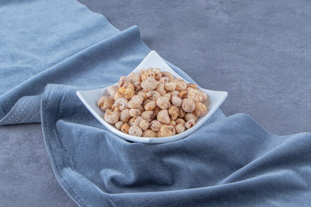 Cornflakes mit Müsli in einer Schüssel auf einem Stück Stoff, auf dem Marmorhintergrund.