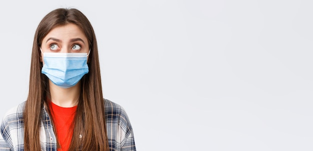 Coronavirus Ausbruch Freizeit auf Quarantäne soziale Distanzierung und Emotionen Konzept Nahaufnahme einer nachdenklichen jungen Frau in medizinischer Maske, Blick in die obere linke Ecke mit Lesezeichen oder Blasengedanken