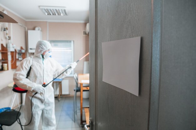 Coronavirus Pandemie. Desinfektor in einem Schutzanzug und Maske sprüht Desinfektionsmittel im Haus oder Büro