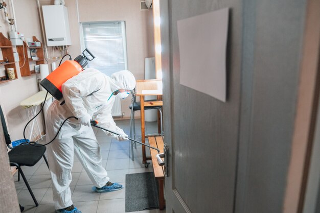 Coronavirus Pandemie. Desinfektor in einem Schutzanzug und Maske sprüht Desinfektionsmittel im Haus oder Büro