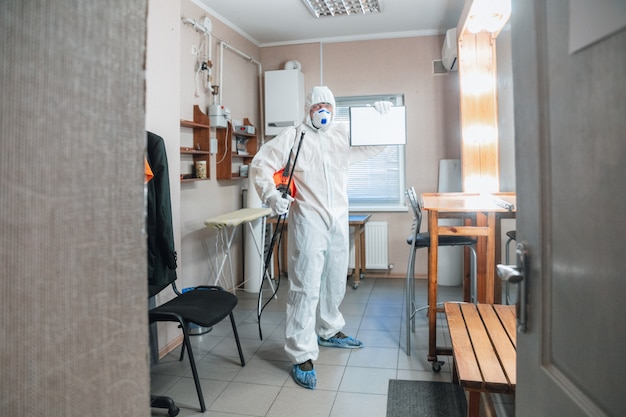 Coronavirus Pandemie. Desinfektor in einem Schutzanzug und Maske sprüht Desinfektionsmittel im Haus oder Büro