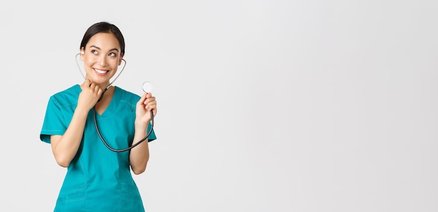 Covid-19, Gesundheitspersonal und Konzept zur Verhinderung von Viren. Lächelnder süßer asiatischer Arzt, weibliche Krankenschwester untersucht die Lungen des Patienten, verwendet Stethoskop, hört genauer zu und steht auf weißem Hintergrund.