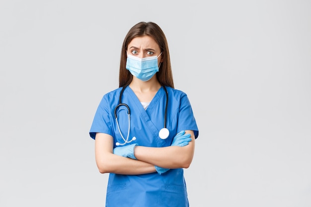 Covid-19, Prävention von Viren, Gesundheit, Gesundheitspersonal und Quarantänekonzept. Skeptische und besorgte Krankenschwester in blauen Kitteln, Stethoskop und persönlicher Schutzausrüstung sehen verdächtig aus