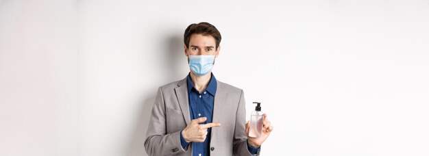 Covid Pandemie und Geschäftskonzept Büroangestellter in medizinischer Maske, der auf eine Flasche Händedesinfektion zeigt