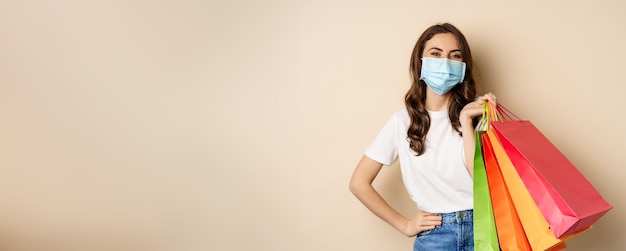 Covid-Pandemie und Lifestyle-Konzept junge Frau posiert in medizinischer Gesichtsmaske mit Einkaufstüten aus