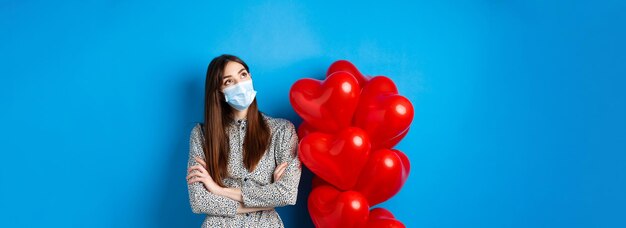 Covid Quarantäne und Gesundheitskonzept verträumtes schönes Mädchen in Gesichtsmaske und Kleid mit Blick auf die obere linke Seite