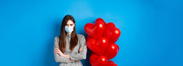 Covid-Quarantäne und Gesundheitskonzept wütende Freundin in medizinischer Maske, die in der Nähe des Valentinstags rot steht