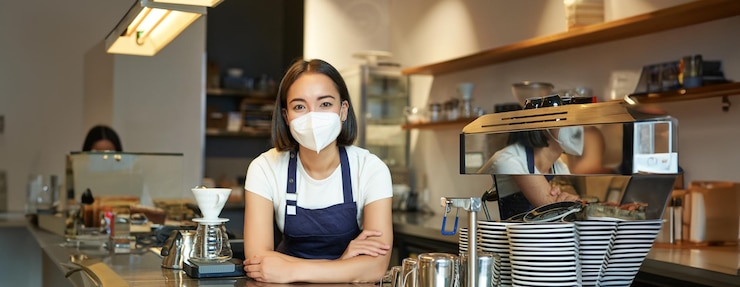 Kostenlose Foto covid und café arbeiten asiatische barista in uniform, die hinter der theke steht und als barkeeperin arbeitet