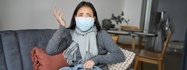 Kostenloses Foto covid- und gesundheitskonzept junge asiatische frau mit medizinischer gesichtsmaske fühlt sich krank und unwohl, wenn sie grippe bekommt