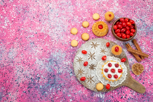 Cremekuchen der oberen entfernten Ansicht mit frischen roten Preiselbeeren zusammen mit Zimtplätzchen auf der süßen Bodenbeere des lila Bodenkekses