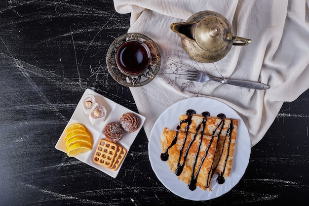 Crepes in einem weißen Teller mit Schokoladensirup und Tee.