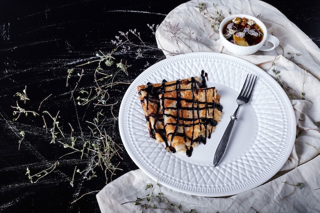 Crepes in einem weißen Teller mit Schokoladensirup und Tee.