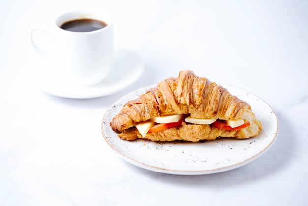 Croissant gefüllt mit Käse und Tomaten und einer Tasse Kaffee