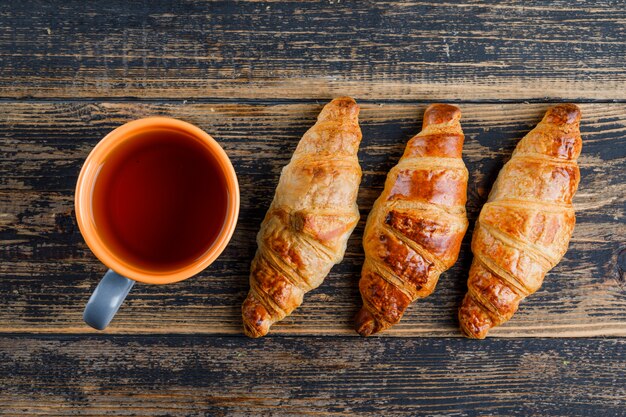 Croissant mit Tasse Tee auf Holztisch, flach liegen.