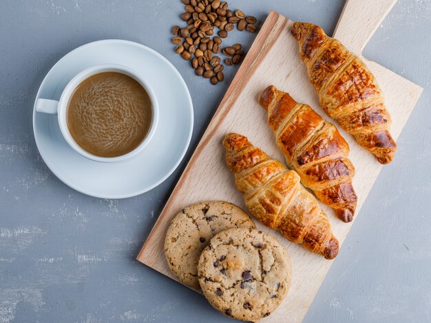 Croissants mit Kaffee und Bohnen, Kekse auf Gips und Schneidebrett, flach liegen.