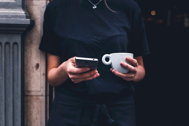 Crop Barista mit Getränk mit Smartphone