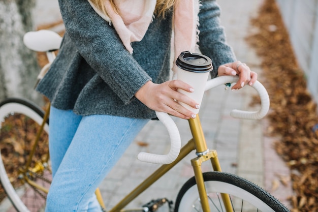 Crop Frau mit Fahrrad und Heißgetränk