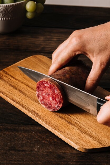 Crop Hände schneiden geräucherte Wurst an Bord