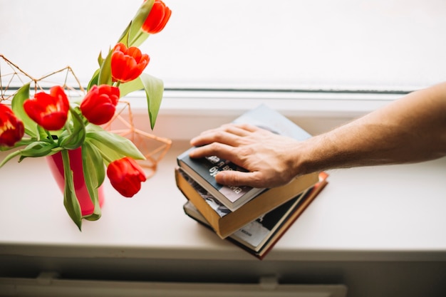 Crop Hand auf Bücher in der Nähe von Blumen