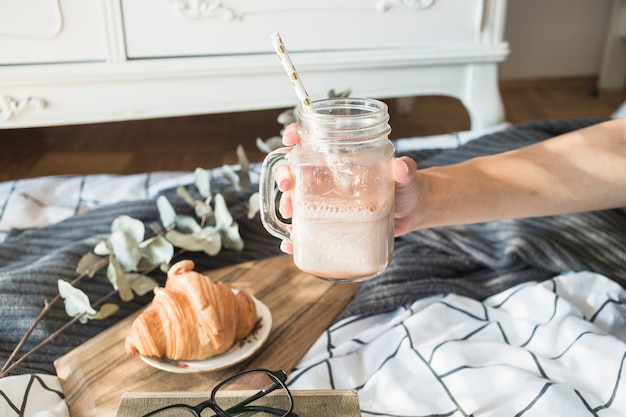 Crop Hand mit Getränk über Bett und Croissant