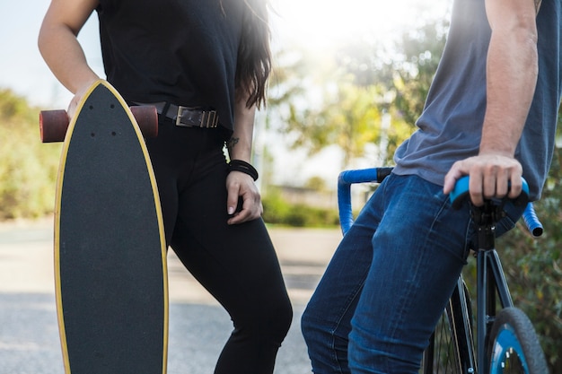 Crop Menschen mit Fahrrad und Longboard