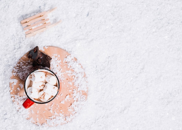 Cup mit Marshmallows in der Nähe von Schokolade auf Stand und Spielzeug Pullover zwischen Schnee