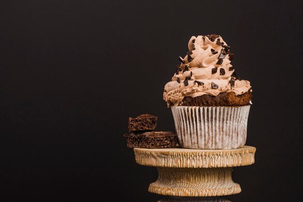 Cupcake auf hölzernem Stand gegen schwarzen Hintergrund