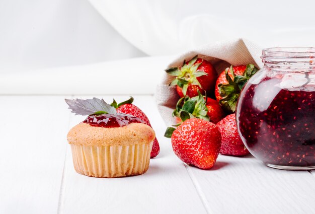Cupcake der Seitenansicht mit Erdbeermarmeladenbasilikum und frischer Erdbeere auf weißem Hintergrund